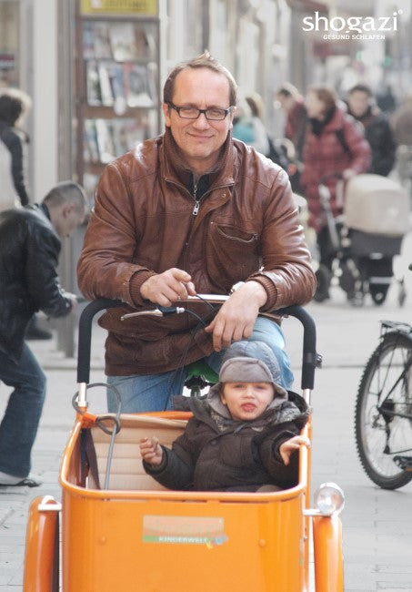 Person mit Kind im Kinderwagen in einer Einkaufsstraße – Symbolbild für den familiengeführten Matratzenhersteller shogazi®