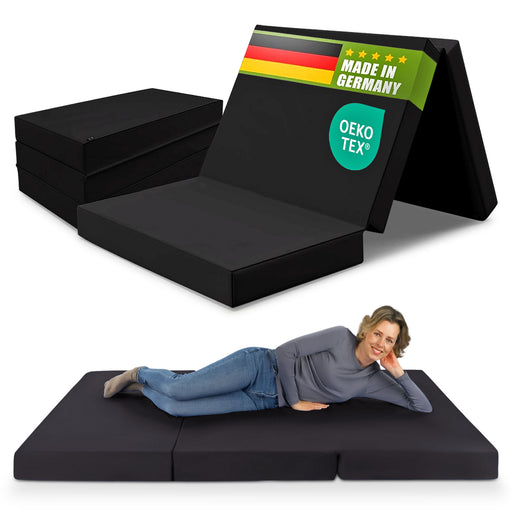 Frau liegt entspannt auf einer schwarzen Klappmatratze 140x200 cm, hergestellt in Deutschland, OEKO-TEX® zertifiziert, mit gestapelten Matratzen im Hintergrund