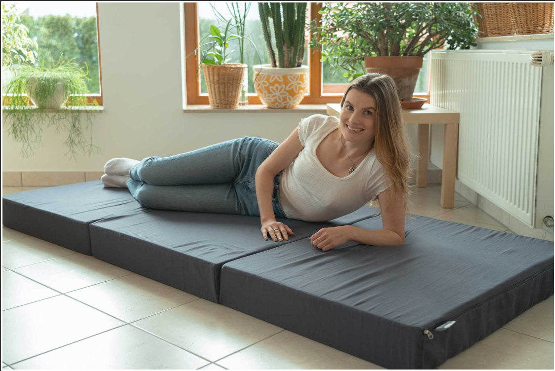 Person liegt auf ausgeklappter 15 cm hoher Klappmatratze aus Kaltschaum und Visco mit waschbarem Baumwollbezug, atmungsaktiv und Made in Germany