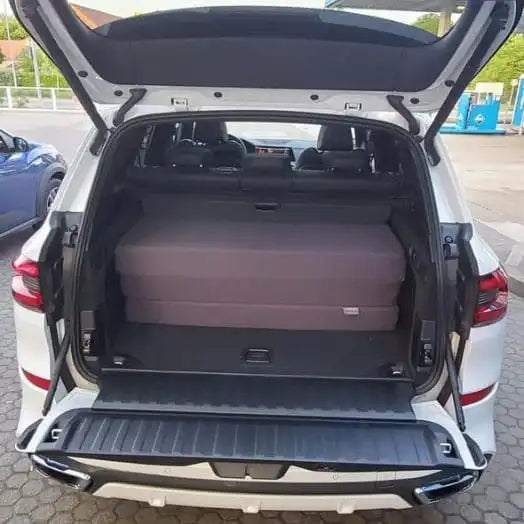 Weißer BMW X5 mit geöffneter Heckklappe, gefaltete Matratze aus orthopädischem Kaltschaum im Kofferraum, made in Germany, Manufaktur seit 2002.