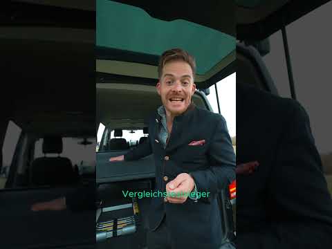 Shogazi Klappmatratze im VW T5/T6/T6.1 Bus – Vergleichssieger! Junger Mann in Anzug präsentiert enthusiastisch die graue Luxus-Faltmatratze im offenen VW California Ocean Campervan. Orthopädischer Kaltschaum-Komfort für VW Bus Camping, Roadtrips und entspannten Schlaf – Made in Germany. shogazi® Top-Matratze für maximalen Liegekomfort!